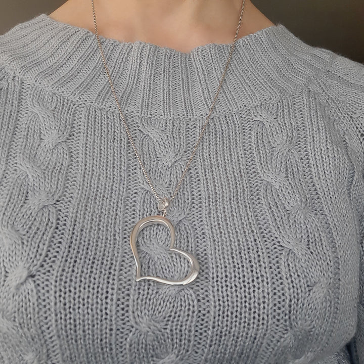 Mujer usando colgante de corazón de plata con look romántico